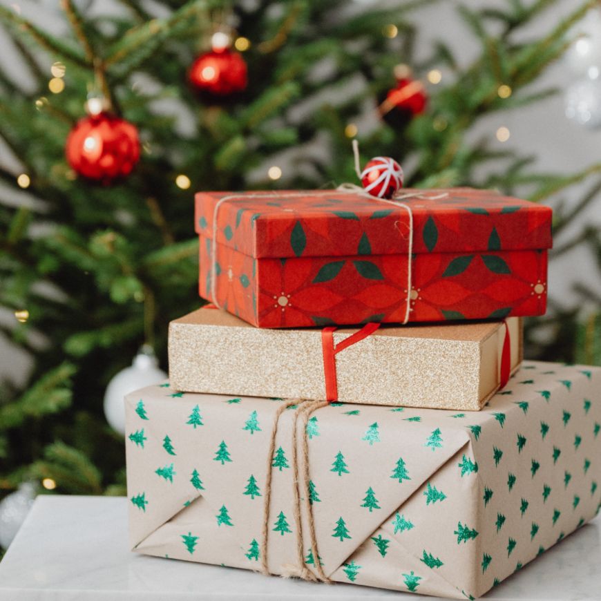 Tres regalos apilados sobre mesa blanca con árbol de Navidad al fondo
