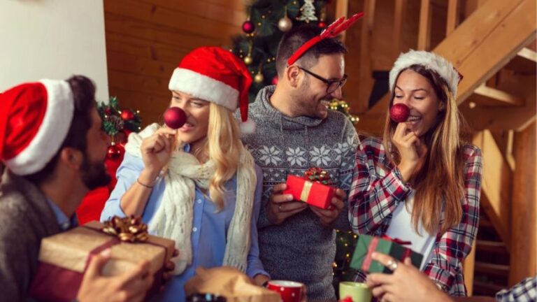 Cuatro amigos con gorros navideños dándose regalos los unos a los otros en casa decorada de Navidad