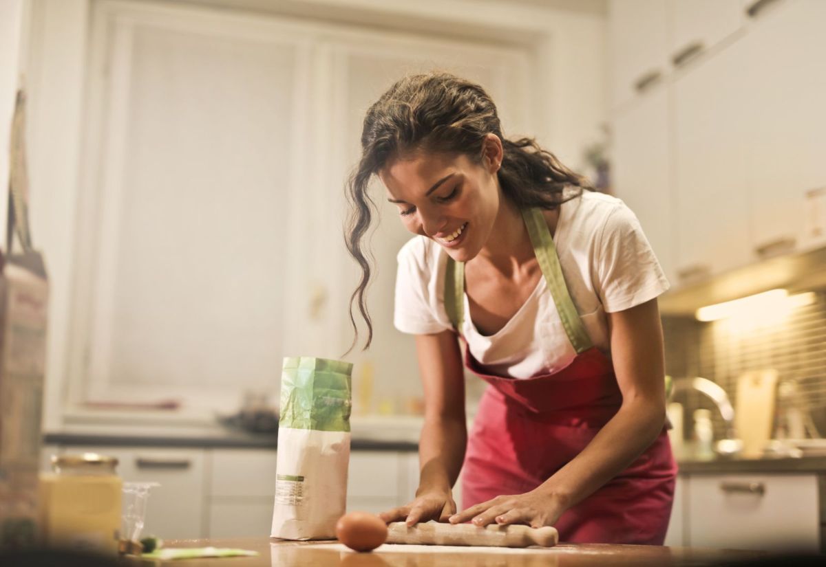 Mujer con actitud feliz cocinando sobre mesa de madera de una cocina blanca