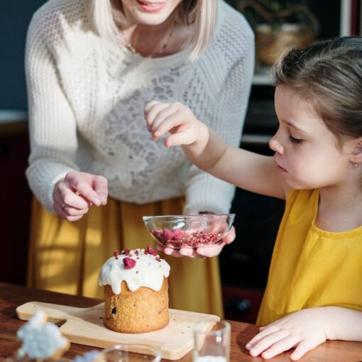 Niña con su madre en la cocina de su casa decorando un pastel