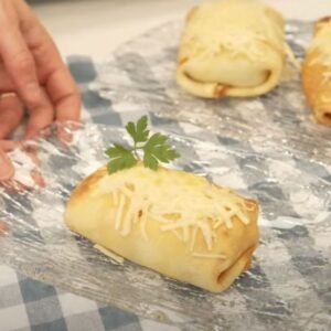 Crep rellena de gambas sobre bandeja de cristal con queso gratinado encima y rama de perejil para decorar