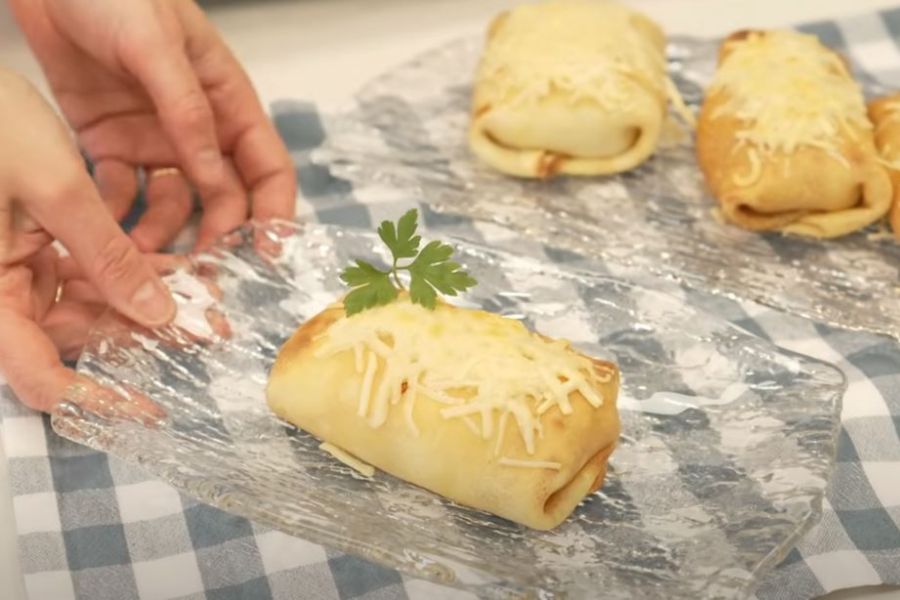 Crep rellena de gambas sobre bandeja de cristal con queso gratinado encima y rama de perejil para decorar