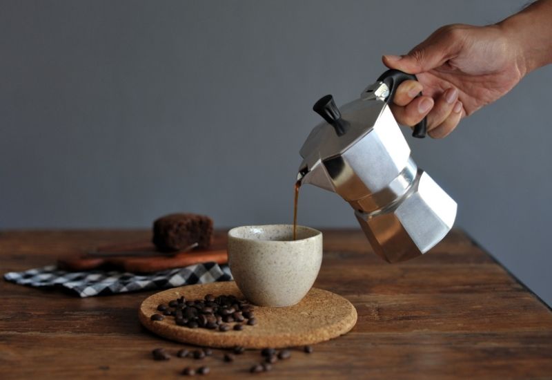 Cafetera italiana en preparación con taza de café recién servido