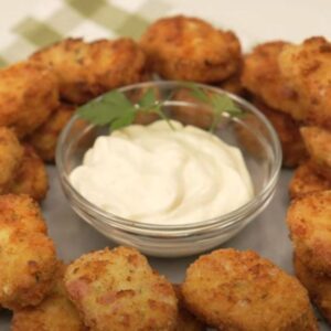Plato lleno de nuggets de pollo con bote transparente circular ubicado en el centro con salsa de color blanco