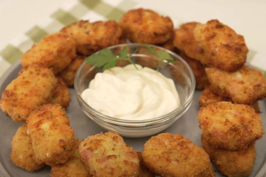 Plato lleno de nuggets de pollo con bote transparente circular ubicado en el centro con salsa de color blanco