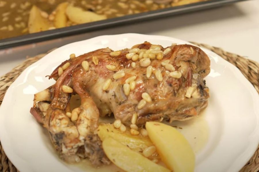 Plato con pierna de cordero asada acompañada de salsa, patatas y piñones