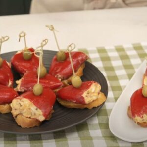 Plato negro y bandeja blanca con pimientos del piquillo rellenos de atún sobre pan tostado y con una aceituna cada uno