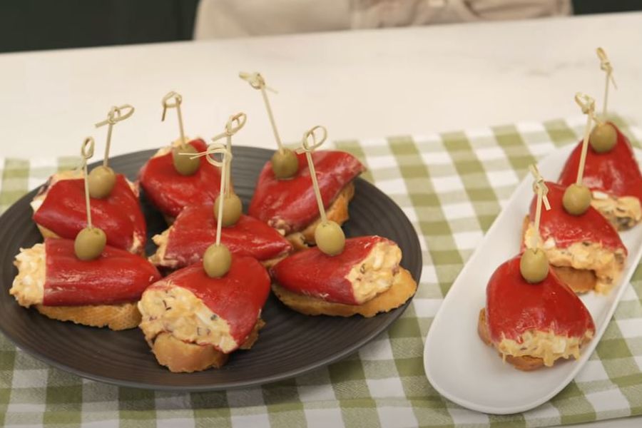 Plato negro y bandeja blanca con pimientos del piquillo rellenos de atún sobre pan tostado y con una aceituna cada uno
