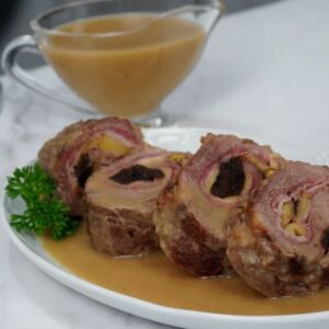 Fuente blanca con cuatro trozos de presa ibérica rellena acompañados de una salsa y perejil a modo decorativo