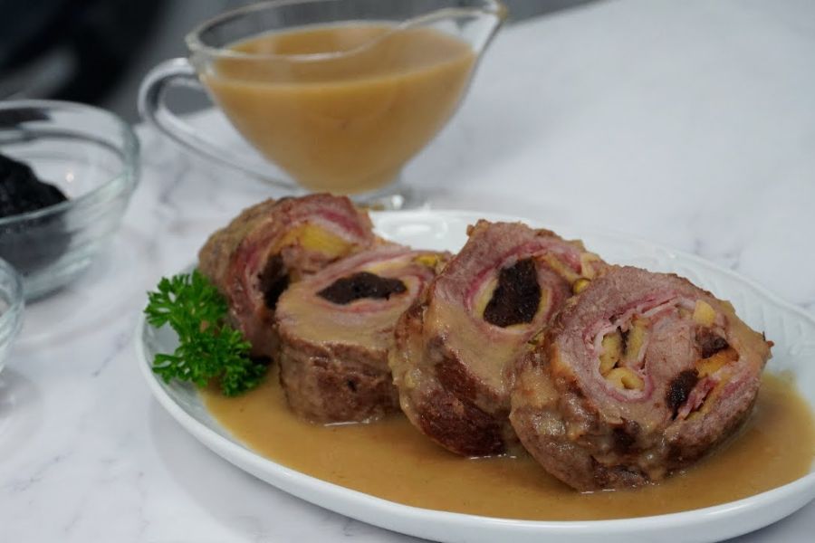 Fuente blanca con cuatro trozos de presa ibérica rellena acompañados de una salsa y perejil a modo decorativo