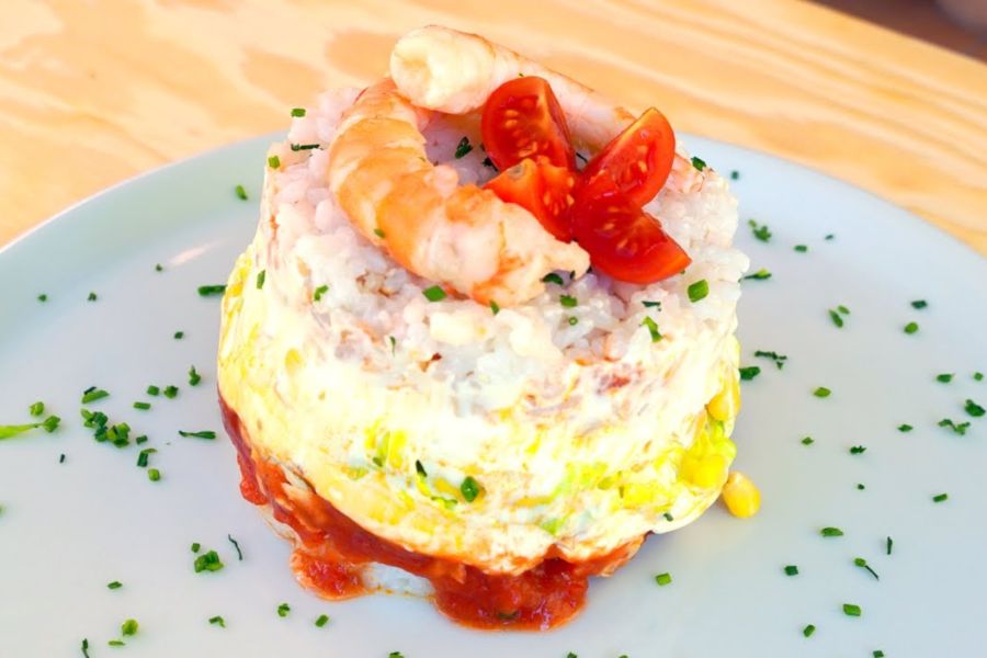 Timbal de arroz frío sobre plato decorado con dos langostinos y cebollino picado