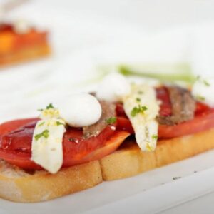 Tosta de anchoa y boquerón con tomate y bolas de mozarella sobre plato blanco