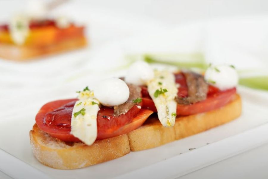 Tosta de anchoa y boquerón con tomate y bolas de mozarella sobre plato blanco
