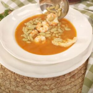 Plato hondo con verdinas en salsa acompañadas de rape y langostinos, servido sobre mantel individual de fibra natural y paño de cocina a cuadros verdes.