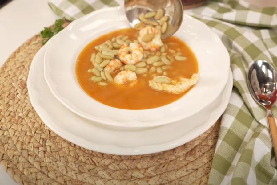 Plato hondo con verdinas en salsa acompañadas de rape y langostinos, servido sobre mantel individual de fibra natural y paño de cocina a cuadros verdes.